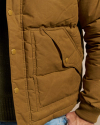 Close-up of a person wearing a brown padded jacket with a buttoned flap pocket and a visible black knitted sweater underneath.