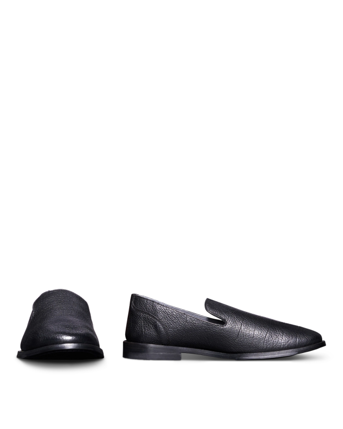 Black leather loafers against a black background, with one shoe standing upright and the other lying on its side.