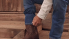Man putting on The Doc cowboy boot under jeans