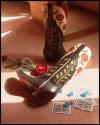 Pair of embroidered cowboy boots, a red rose, blue dice, and playing cards placed on a carpeted floor in warm sunlight.