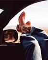 Person wearing red cowboy boots and blue jeans with their feet resting out of a car window; desert landscape visible outside.