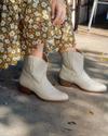 Woman in a dress wearing the Tecovas Paige boots in the color bone.