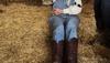 Farmer in overalls and cowgirl boots sitting on hay