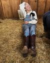 Farmer in overalls and cowgirl boots sitting on hay