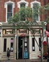 Front view of French’s Shoes & Boots store with a large tree partially obscuring the entrance and a person standing near the door on a city sidewalk.
