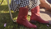 A person wearing red leather boots and a black and white checkered skirt sits outdoors on the grass.