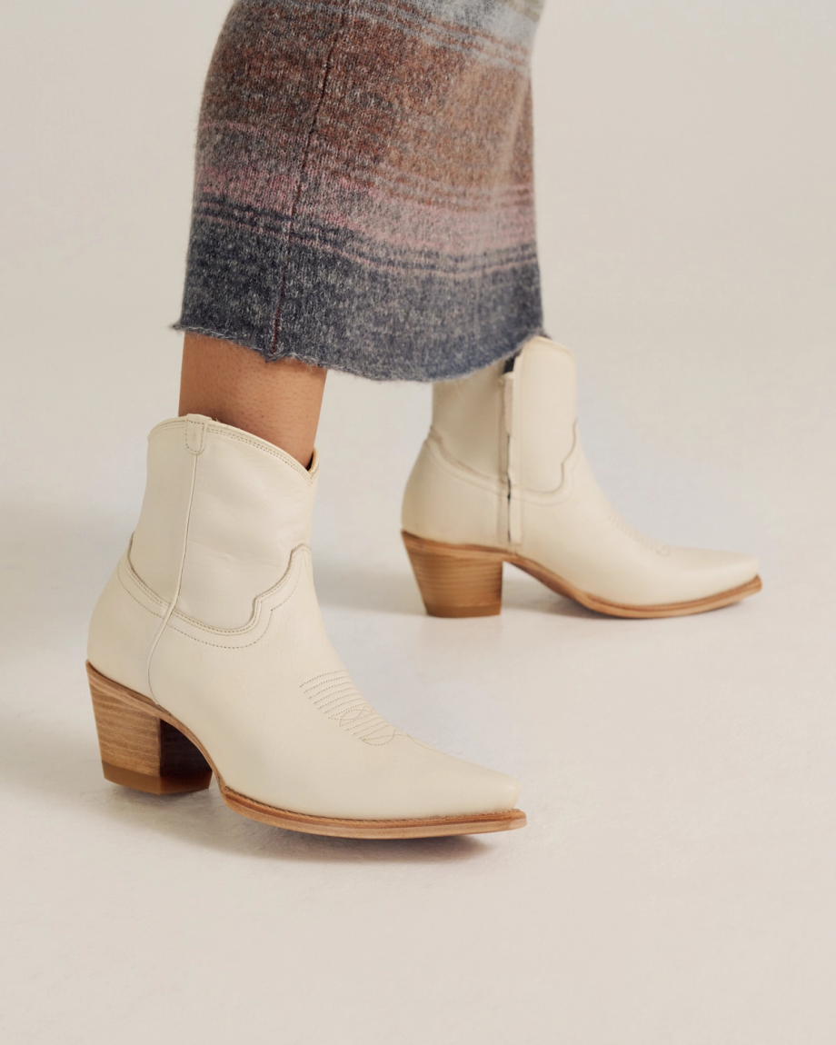 A person wearing a long, striped skirt and off-white, mid-calf western boots with side zippers and wooden heels.