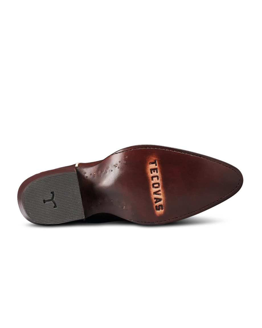 The Jolene in Truffle Cowhide. The underside of a brown leather shoe crafted from The Jolene Cowhide, with the word “Tecovas” stamped near the pointed toe and a black rubber grip on the heel.