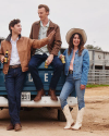 Three people dressed in casual western attire stand at the back of a pickup truck, holding drinks and smiling. A man in the center gestures with his hand. A ranch backdrop is visible.