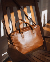 Bartlett Slim Briefcase in Cognac resting on a wooden chair