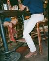Two people sit at a wooden table in a casual setting; one wears red cowboy boots and denim shorts, the other white pants, brown boots, and a navy shirt. Only their lower bodies are visible.