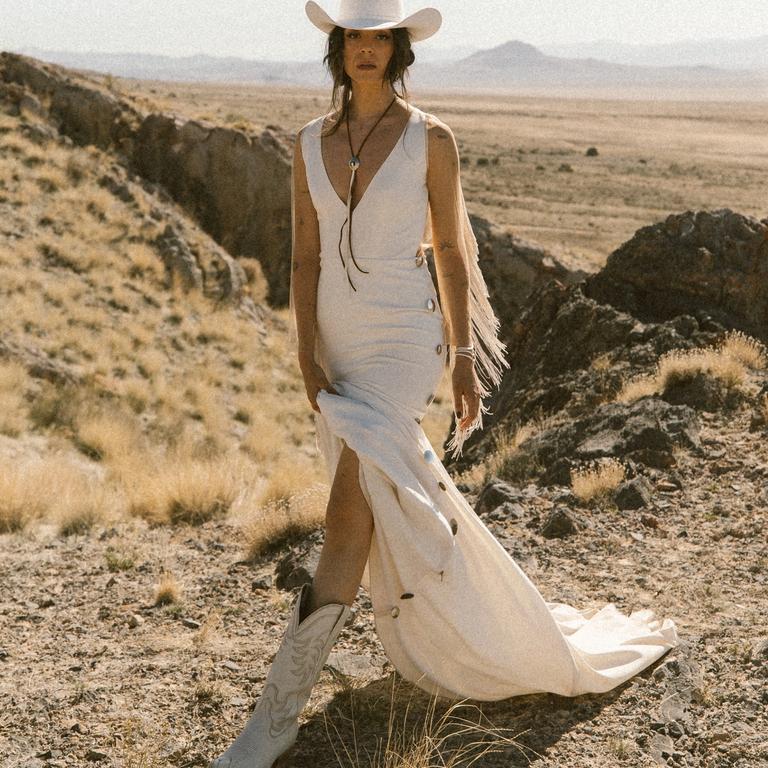 a woman in a field in a wedding dress, white cowgirl boots and a white cowboy hat