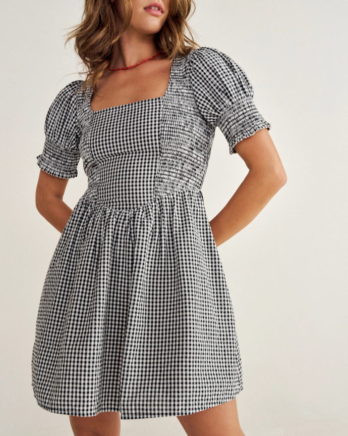 A woman in a black and white checkered dress with puffed sleeves stands against a plain background.