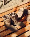 A pair of brown cowboy boots with decorative stitching sit on a wooden pallet in sunlight.