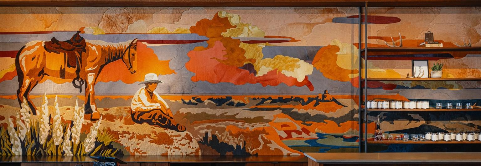 Colorful mural of a cowboy and horse in a Southwest landscape adorns a cafe wall, with wooden counters and shelves displaying cups.