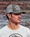 Man wearing the olive trucker hat in front of a metal wall
