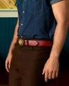 A person wearing a short-sleeve denim shirt, brown pants, and a red belt with a decorative buckle, standing indoors.