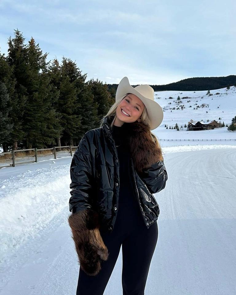 A woman in a cowboy hat **poses** in the snow.