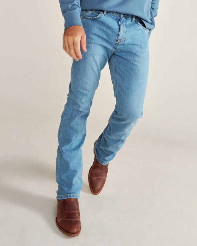 A person wearing light blue jeans, a blue long-sleeve shirt, and brown leather boots stands on a light-colored floor.