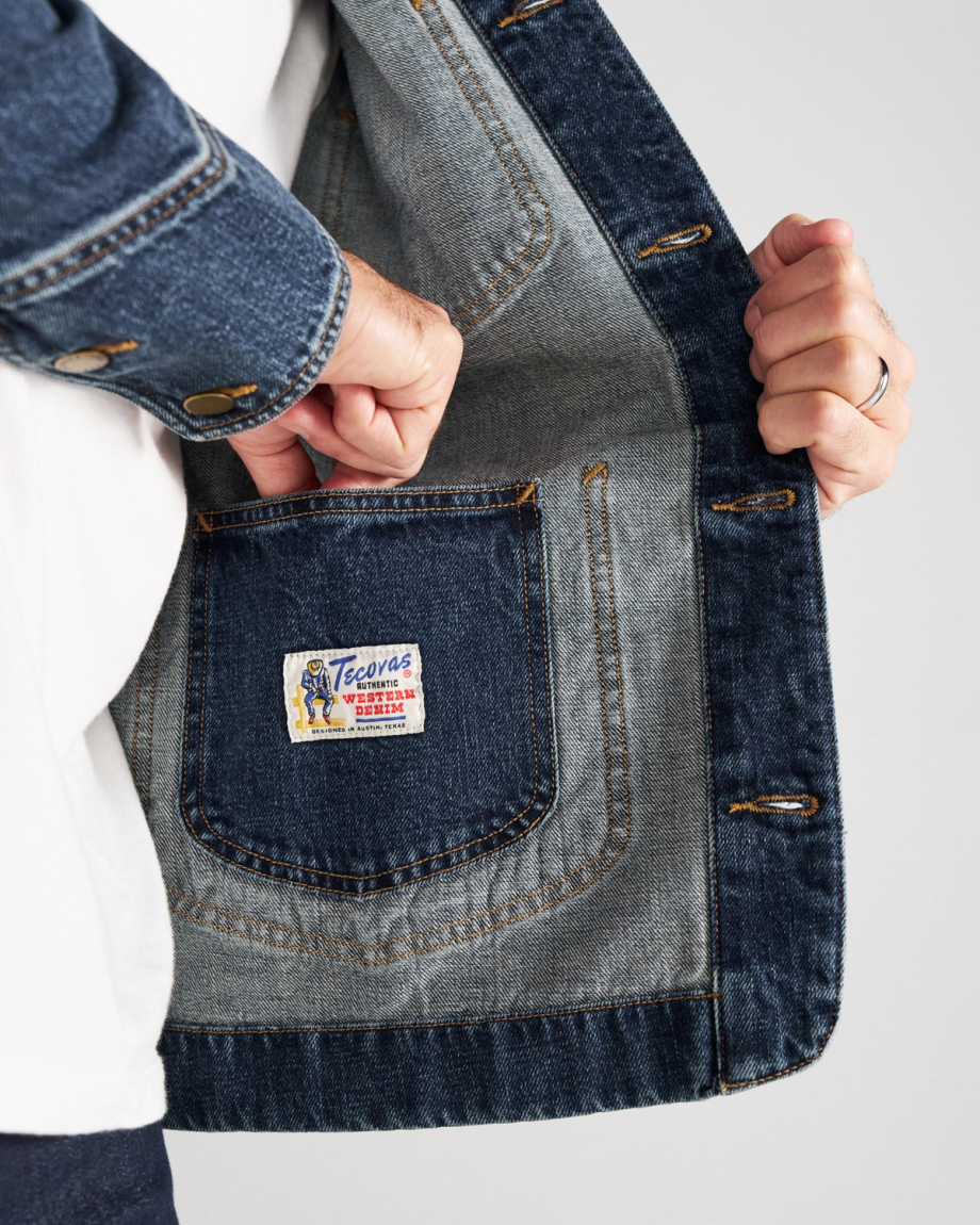 A person opens a denim jacket to show an inside pocket with a label that reads “Tecovas Western Goods.”.