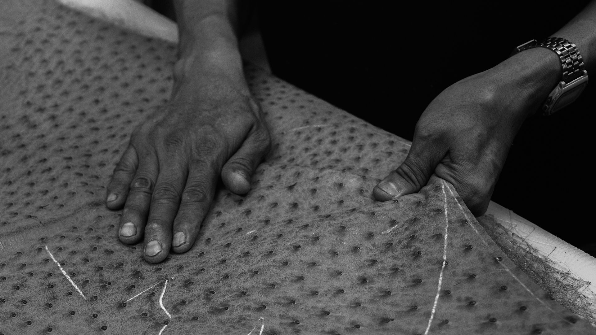 A person’s hands work with a textured, spotted fabric on a flat surface; one hand stretches the material while the other holds it steady.