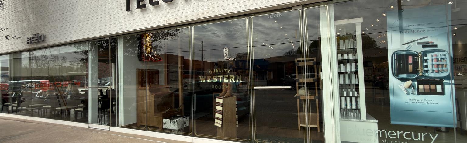 Exterior of a Tecovas store with large glass windows and adjacent Bluemercury signage; sidewalk and parked cars visible outside.