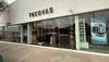 Exterior of a Tecovas store with large glass windows and adjacent Bluemercury signage; sidewalk and parked cars visible outside.