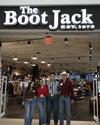 Four people stand in front of The Boot Jack store entrance, smiling, under a sign with "EST. 1976". The store interior is visible behind them.