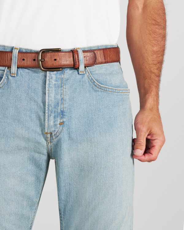 Light-wash blue jeans with a brown leather belt and a brass buckle worn by a person in a white t-shirt.