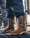 Person wearing worn leather boots and jeans stands on a wet metal grate, surrounded by falling water droplets.