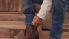 Man adjusting jeans over his brown cowboy boots