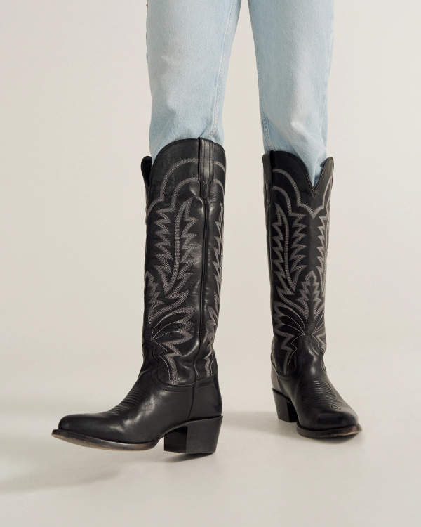 A person wearing light blue jeans and black western cowboy boots stands on a light-colored surface.