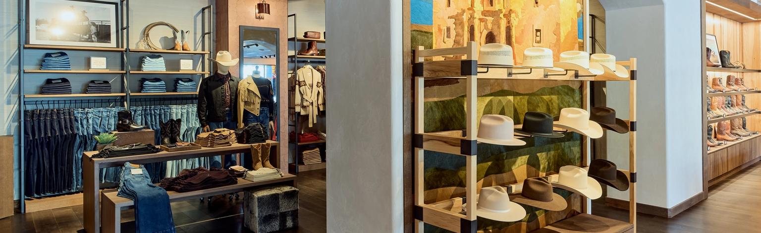 A store interior with shelves displaying hats and clothing. A large mural depicting a desert scene is on the wall. The ceiling features wooden beams.
