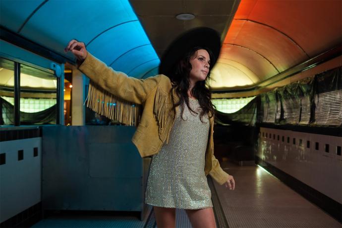 Whitney in a cowgirl hat, fringe jacket and dress