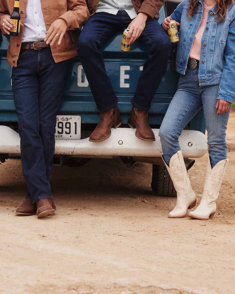 Men and woman in cowboy boots sitting and leaning on a blue pickup truck.