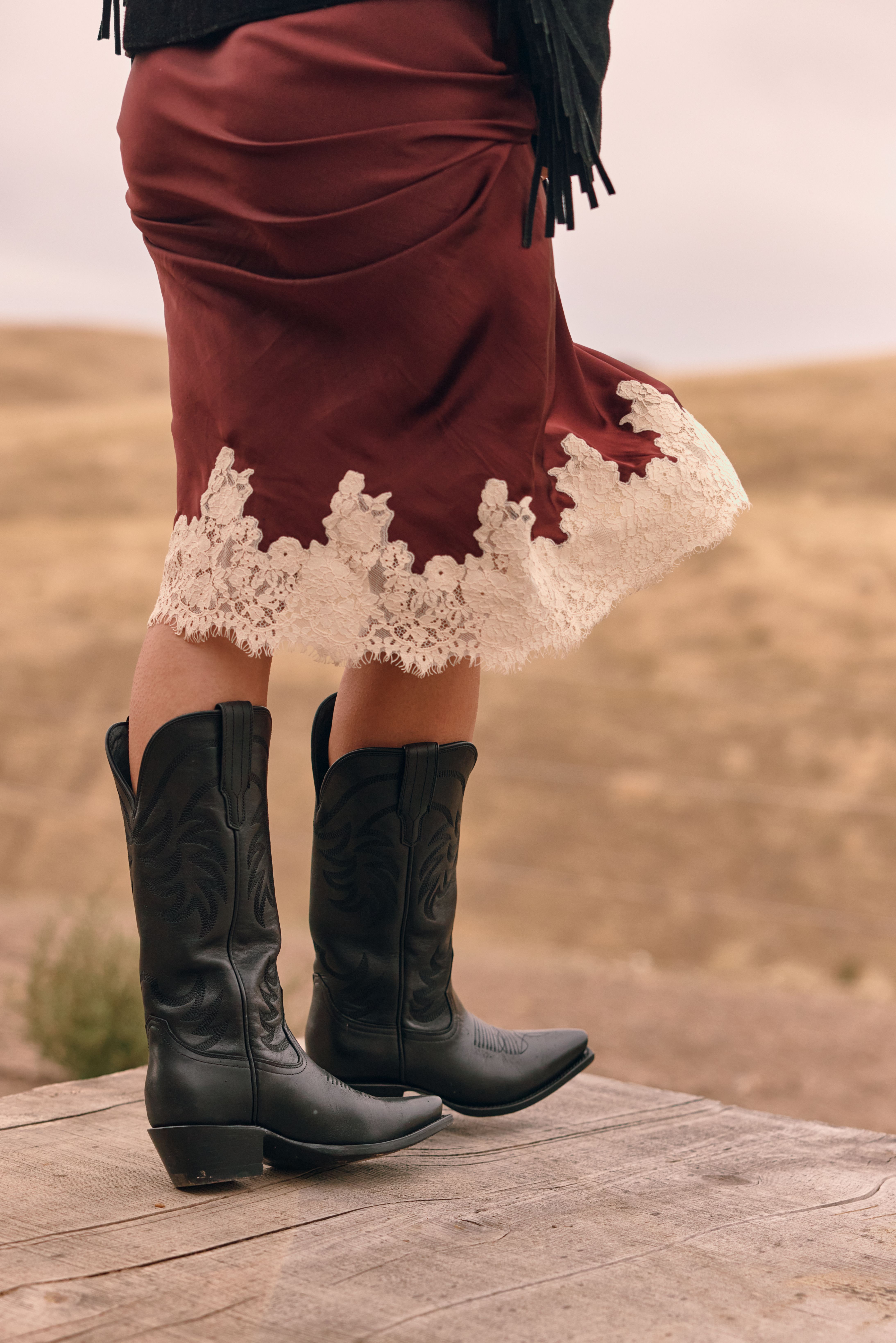 Person sitting wearing red cowboy boots with floral designs, blue denim skirt, and a white top.