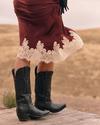 Person sitting wearing red cowboy boots with floral designs, blue denim skirt, and a white top.