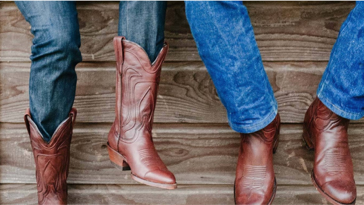 Two people wearing cowboy boots leaning against a wooden wall.