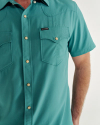 A person wearing a teal short-sleeve button-up shirt with two chest pockets.