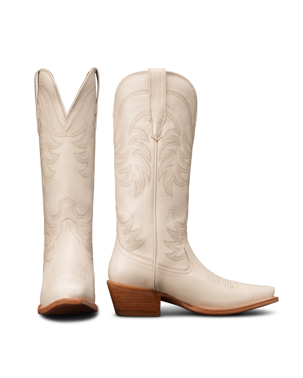 Two white cowboy boots with decorative stitching, showing side and rear views. They have brown stacked heels and pointed toes.