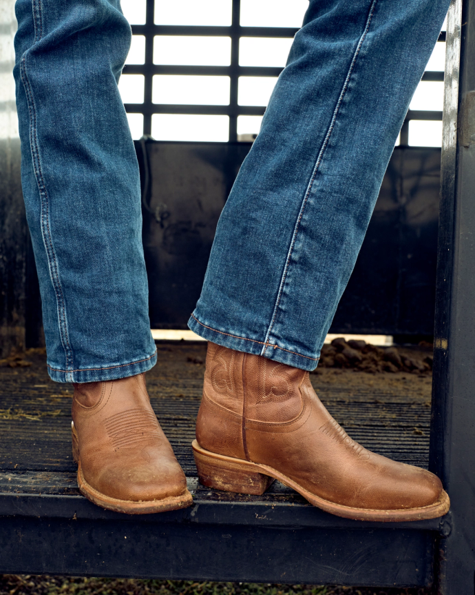 Person wearing blue jeans and brown boots standing on a metal step.