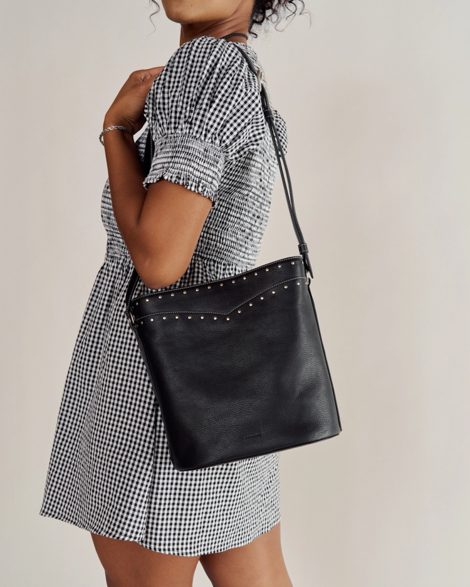 Person wearing a black and white checkered dress holds a black shoulder bag with silver studs against a plain background.