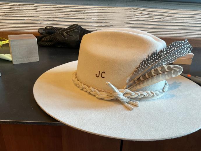 A woman wearing a beige cowboy hat with "rh" initials stands in front of a store window with the word "howdy" displayed.