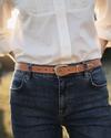 Close up of woman's waist wearing blue jeans and tan three piece belt
