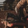 A person wearing cowboy boots, jeans, and chaps mounts a red ATV in a dirt arena.