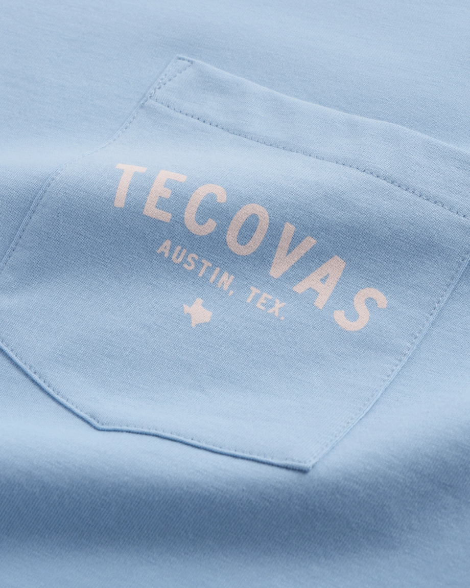 Close-up of a light blue shirt pocket with the words "TECOVAS AUSTIN, TEX." and a small Texas outline printed in white.