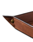 Close-up of a brown leather tray with stitched edges and a brass snap button in the corner.
