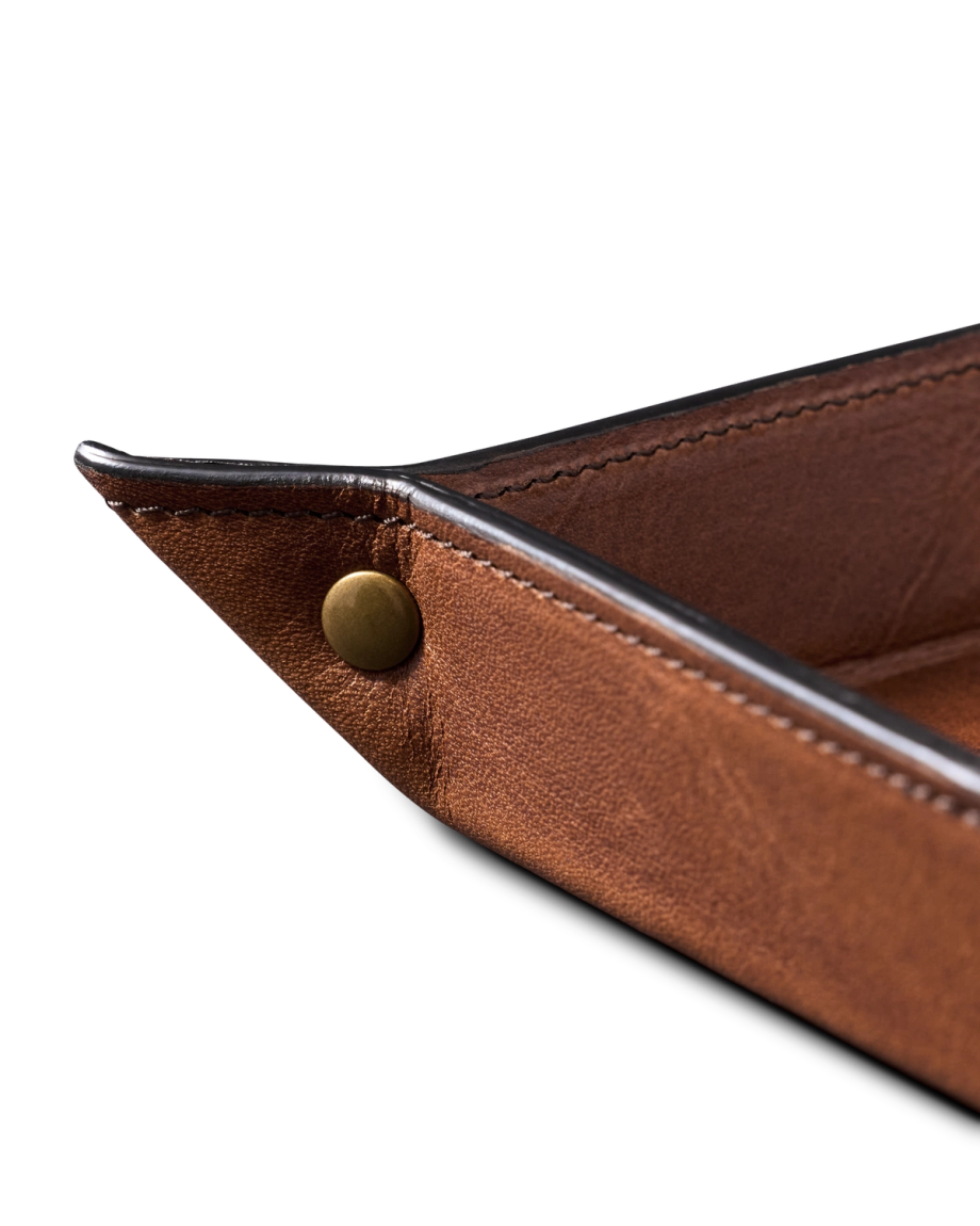Close-up of a brown leather tray with stitched edges and a brass snap button in the corner.