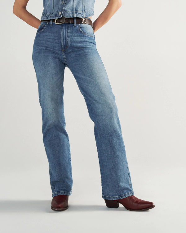 Person wearing blue jeans, a tucked-in denim shirt, a black belt, and burgundy cowboy boots, standing against a plain light background.