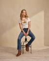 Woman on metal stool wearing Tecovas graphic tee, denim jeans and brown boots.